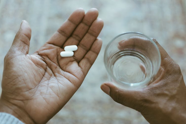 Two white pills in one hand and a glass of water in the other